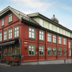 Punainen hotellirakennus jossa vihreät ikkunan karmit ja toisessa päädyssä rakennusta mustat markiisit ja kasvikoristeita.