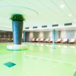 Kylpylän allasosasto, jossa vihreä uima-allas ja sen reunalla aurinkotuolit